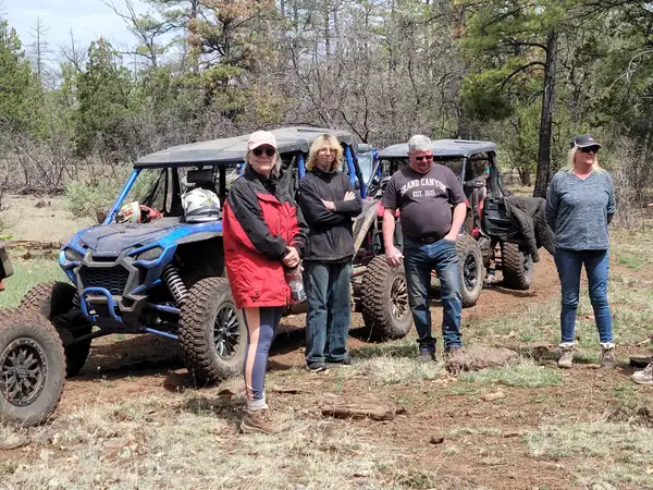Riders standing beside their side-by-sides on a pine forest trail