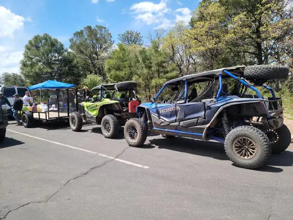Side-by-sides lined up behind a support trailer with a shade canopy at a group stop