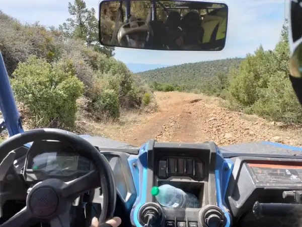 Driver's-eye view from a side-by-side heading down a rocky trail through juniper hills